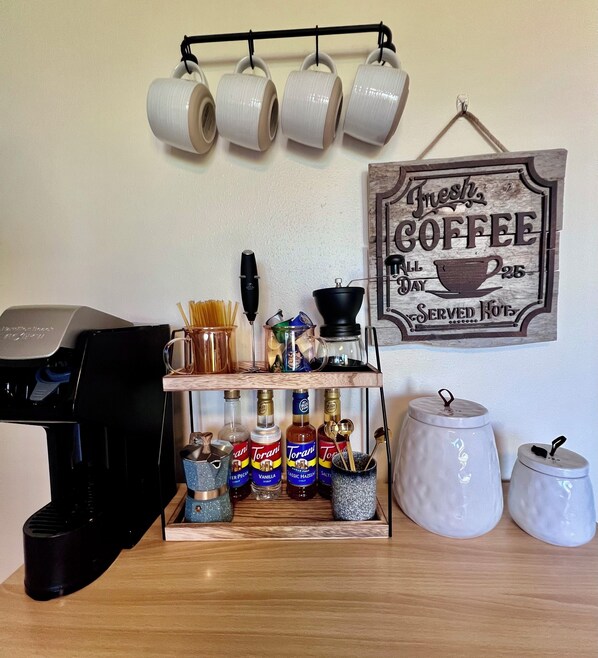 A coffee station with a coffee machine, mugs, Torani syrups, and a sign that reads "Fresh Coffee Served Hot".