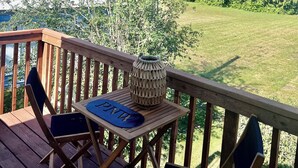 Un terrazzo in legno con tavolo e sedie, affacciato su una zona verde e alberi.