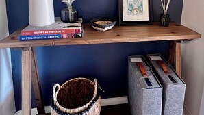 Una scrivania in legno con uno specchio, libri, un vaso, una cornice e un cesto di vimini.