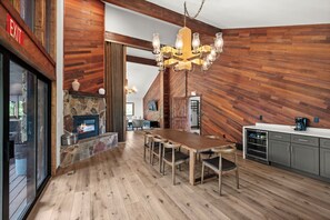 A spacious kitchen with a large wooden table, a stone fireplace, and a modern coffee machine.