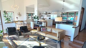 A spacious living area with a sofa, armchairs, and a coffee table. A kitchen is visible in the background with modern appliances and a dining area.