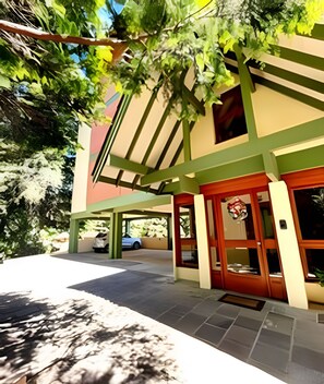 A building with a green and beige facade, a covered entrance, and a parked car in the background.