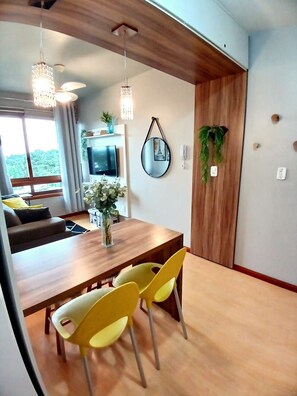 Un espacio habitable moderno con una mesa de comedor de madera, sillas amarillas, un televisor y un amplio ventanal con vistas a la vegetación.