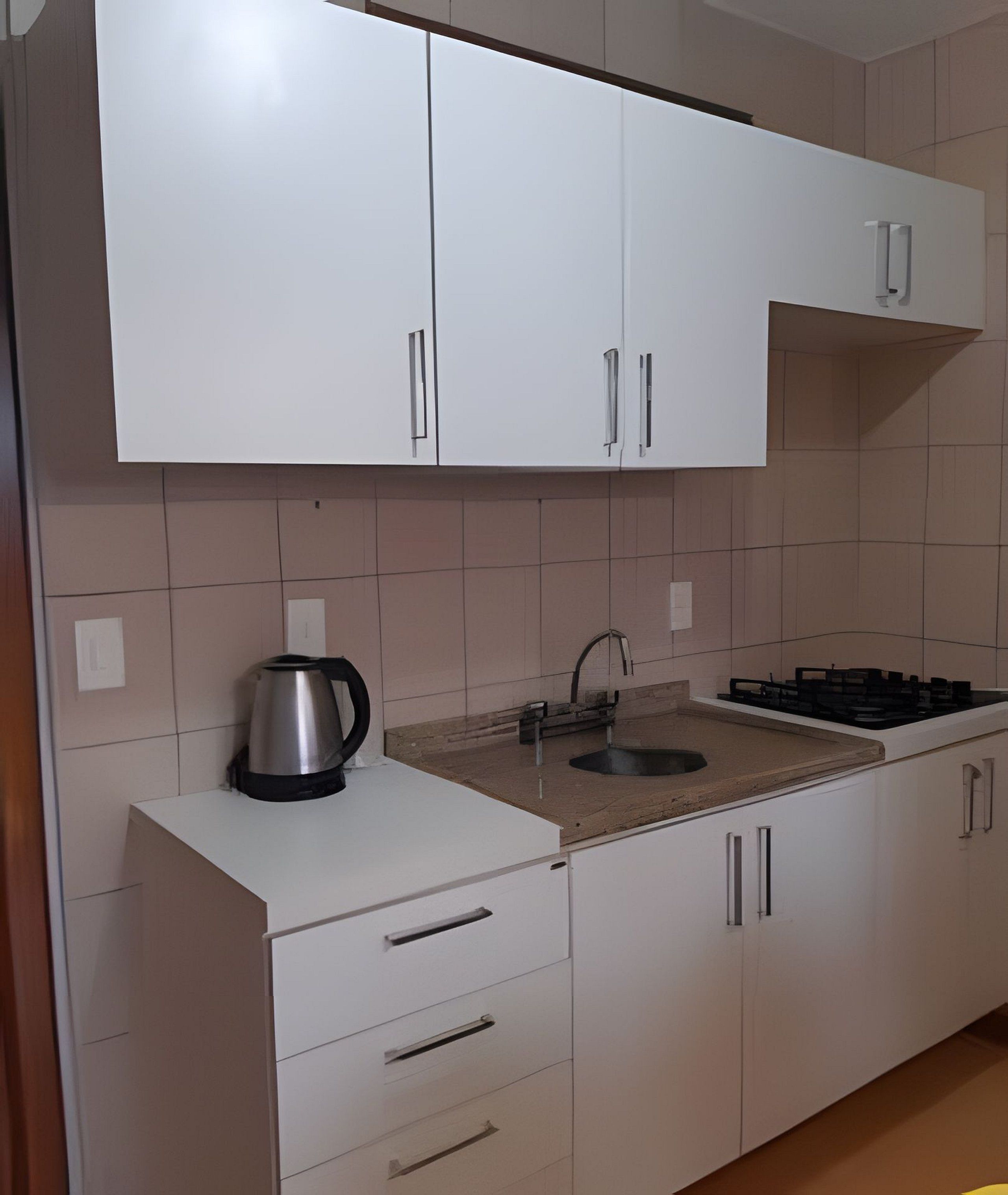 Una cocina con alacenas blancas, un hervidor de acero inoxidable, un lavamanos y una estufa a gas.