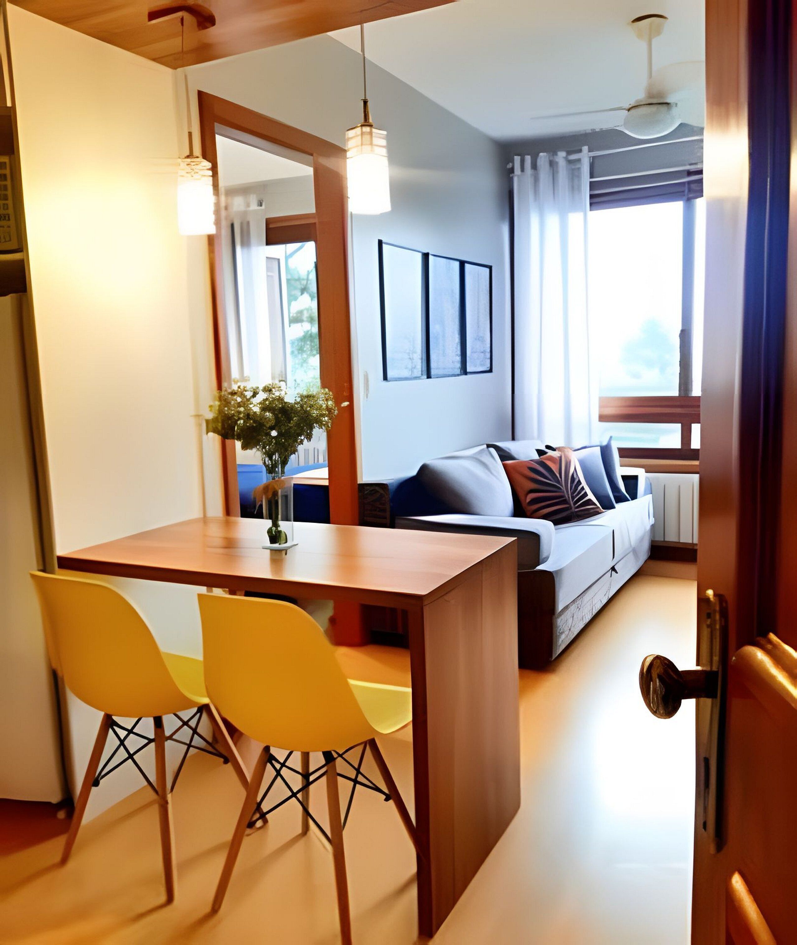 A modern living room with a wooden dining table, yellow chairs, a sofa with cushions, a large window, and a ceiling fan.