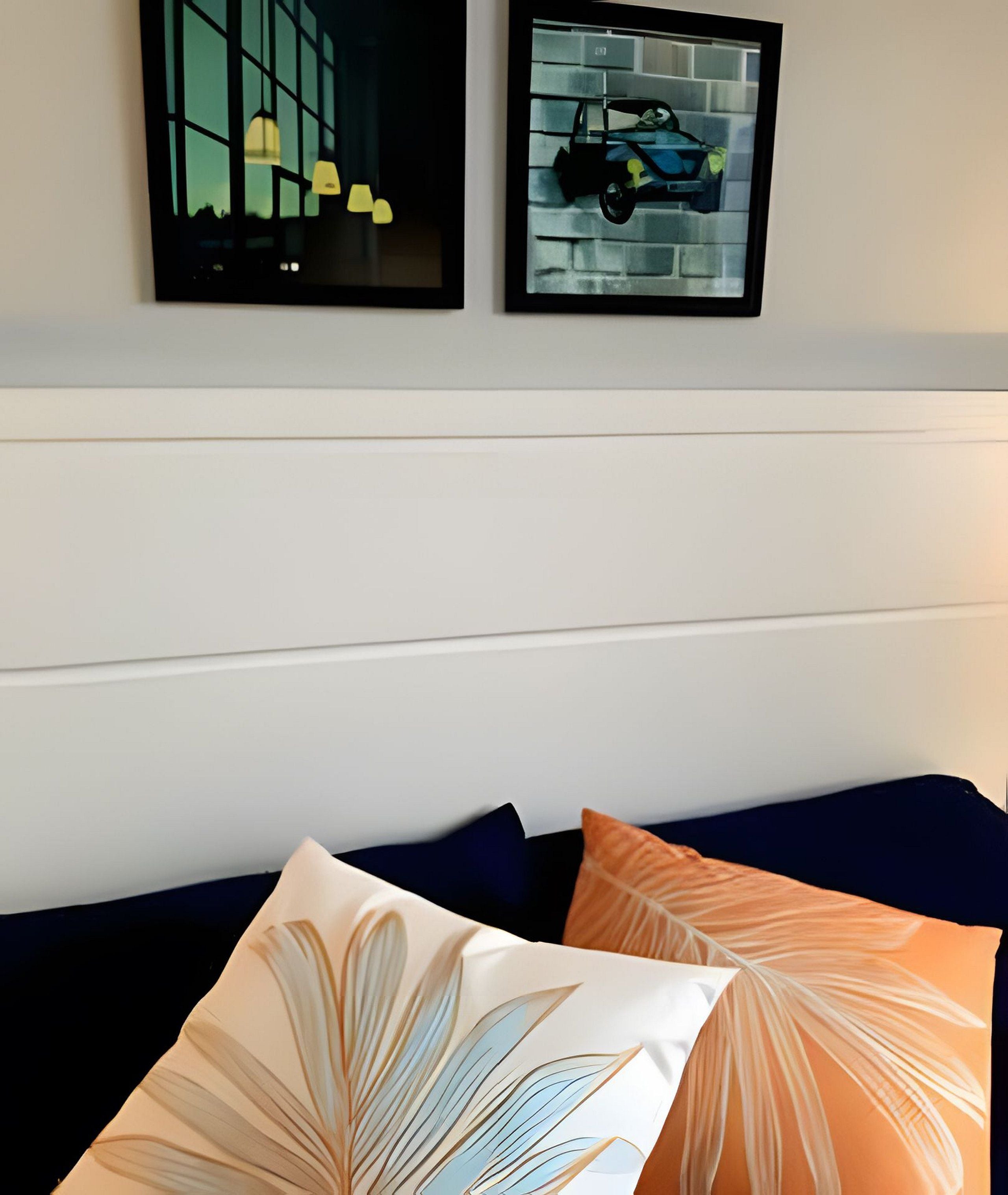 Una habitación con una cama, dos almohadas con motivos de hojas y dos cuadros en la pared.