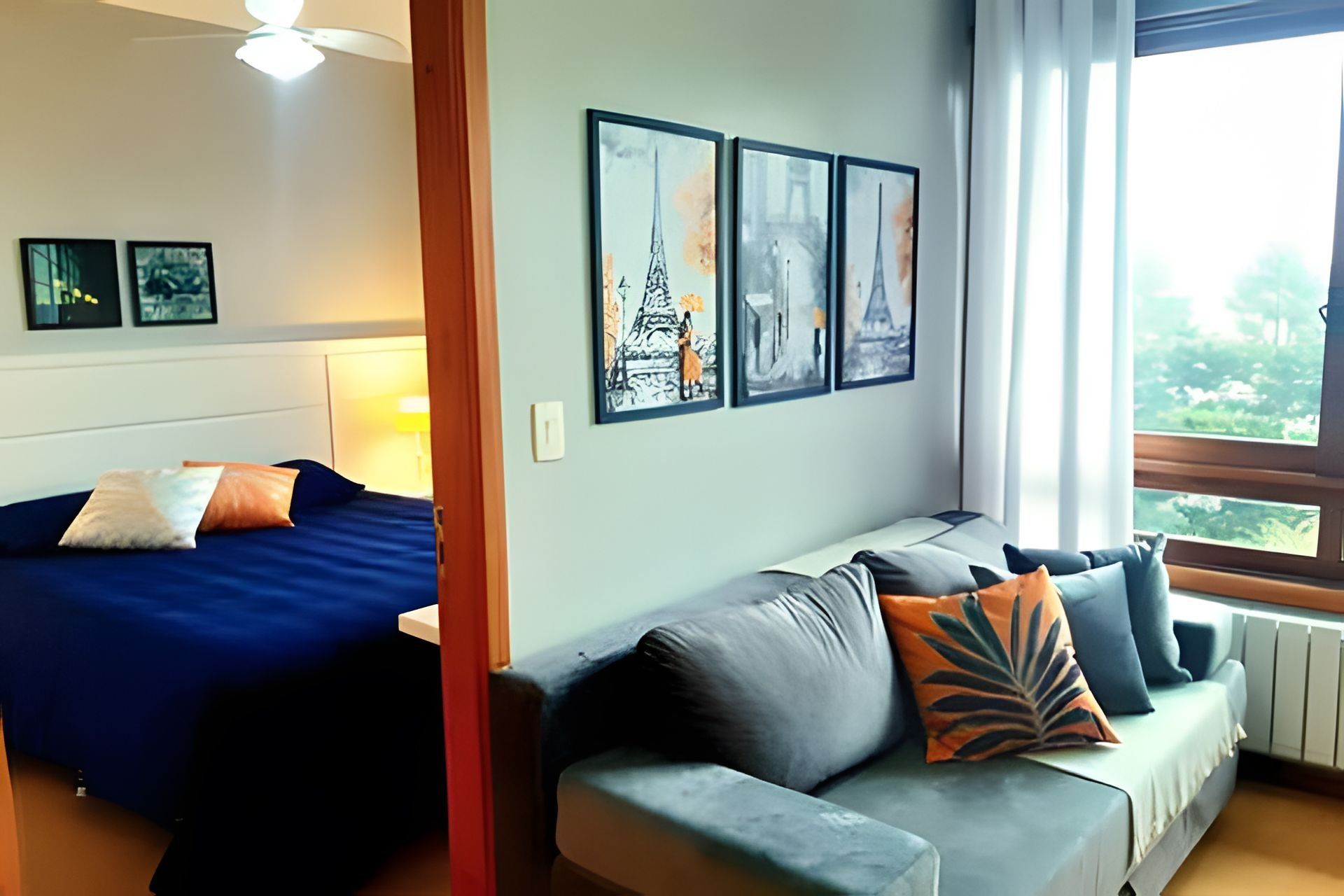 A room with a bed, a sofa, and three framed pictures of Paris landmarks.