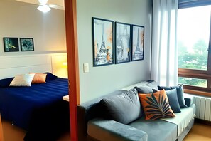 Una habitación con una cama, un sofá y tres cuadros con imágenes de monumentos parisinos.