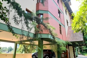 A multi-story building with a green and red facade, a covered parking area, and trees.