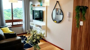 Un soggiorno moderno con una TV su un mobile bianco, uno specchio rotondo e una pianta in vaso.