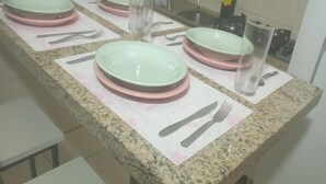 Een keuken met granieten aanrecht, witte barkrukken en een lange eettafel gedekt met borden, bestek en glazen.