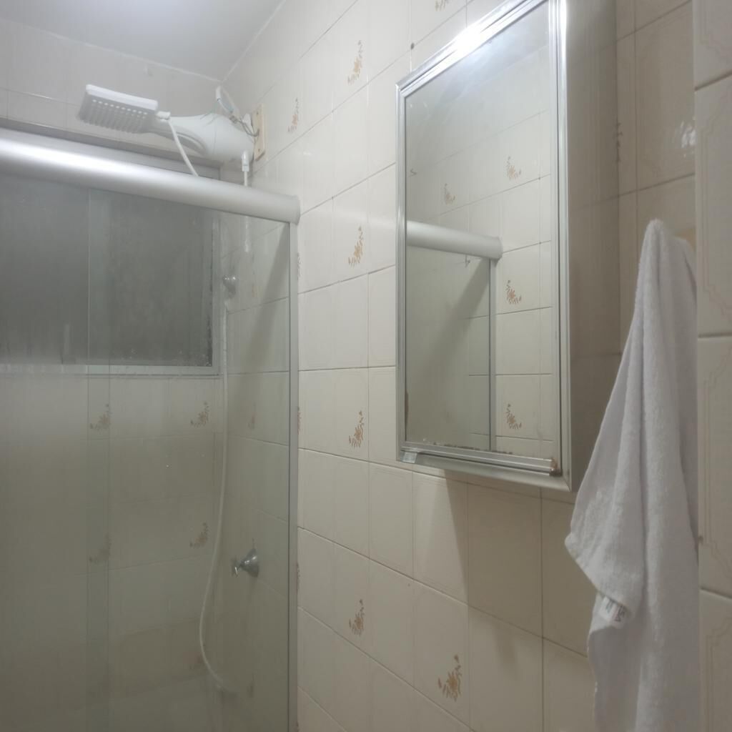 Un baño con azulejos blancos, cabina de ducha de vidrio, una toalla colgada en la pared y un espejo.