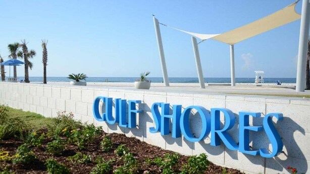Un panneau indiquant « Culey Shores », offrant une vue dégagée sur la plage et les palmiers en arrière-plan.