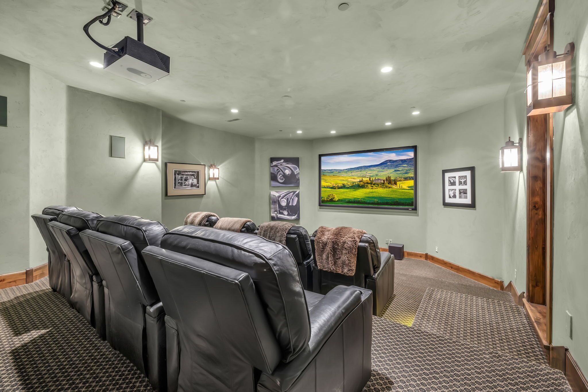 Une salle de cinéma privée équipée de fauteuils en cuir inclinables, d’un grand écran et de tableaux encadrés aux murs.