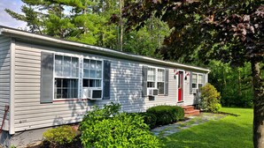 Une maison de plain-pied avec une porte rouge, de nombreuses fenêtres et un appareil de climatisation.