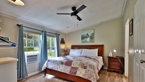 Une chambre à coucher avec un lit en bois, un ventilateur de plafond, une table de chevet et une fenêtre avec des rideaux.