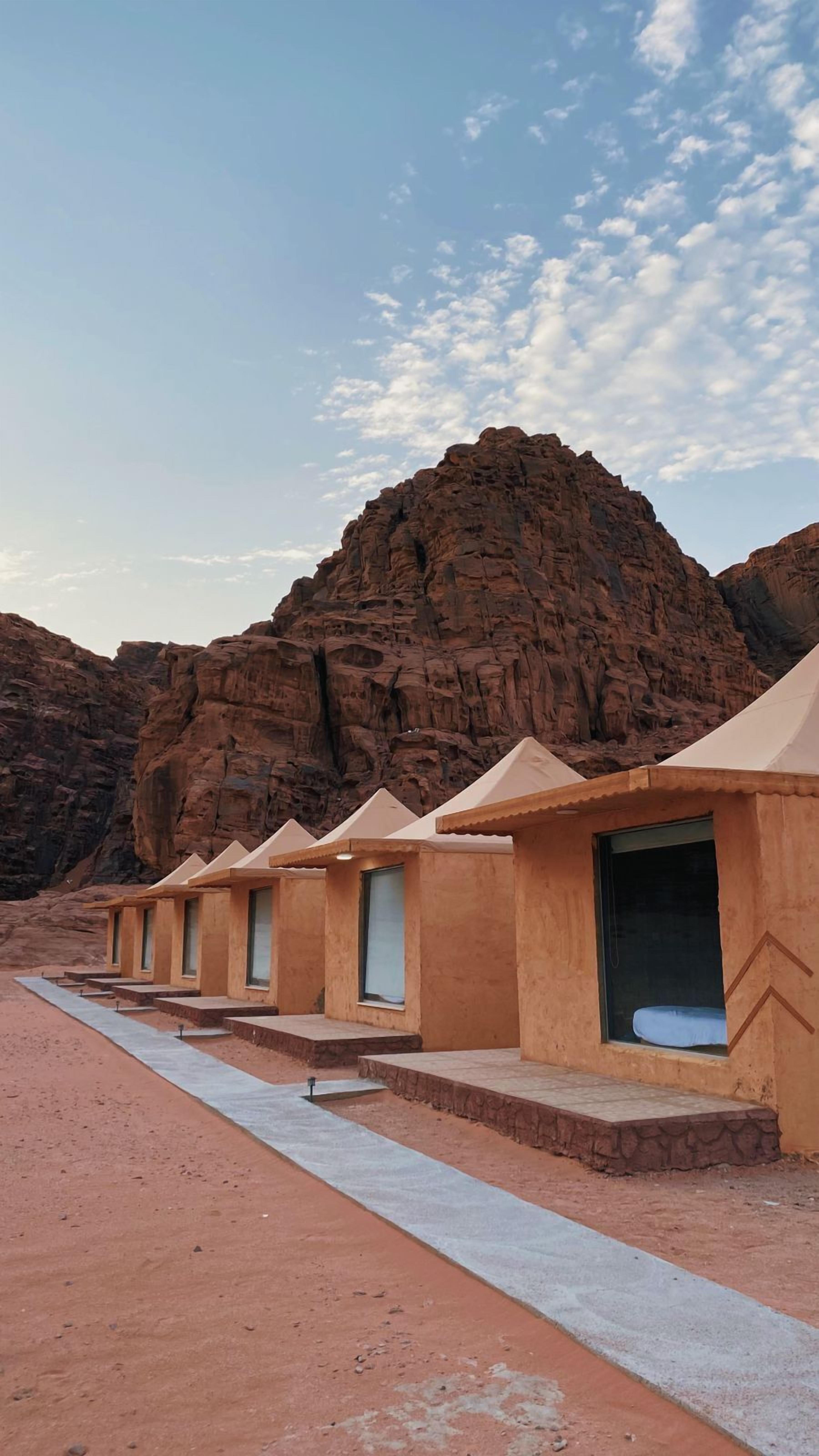 A row of simple, single-room structures with windows and a concrete pathway in a desert setting.