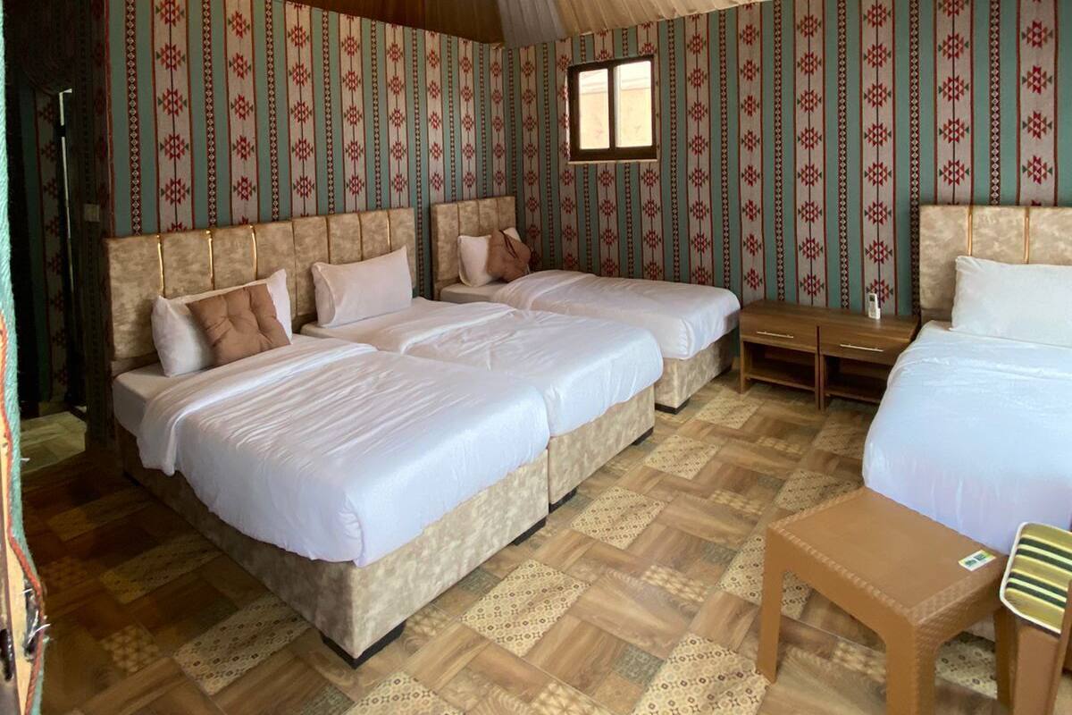 Une chambre avec trois lits, une petite table et un papier peint à motifs.
