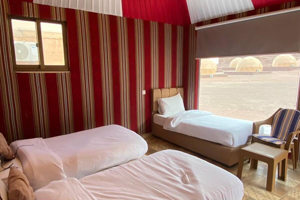Une chambre aménagée comme une tente, avec deux lits, des murs à rayures et une vue sur le désert.