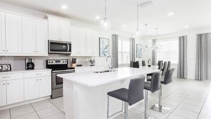 Une cuisine moderne avec des meubles blancs, un îlot central doté de tabourets, un four à micro-ondes, une cuisinière et un coin repas avec des chaises et une table.