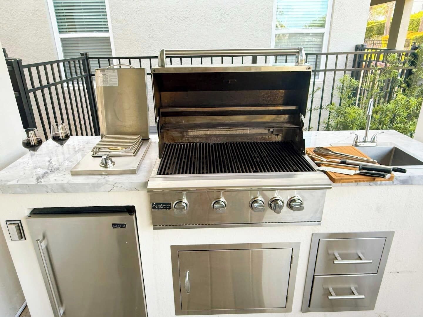 An outdoor kitchen with a grill, a sink, and a refrigerator.