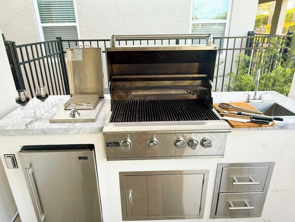 An outdoor kitchen with a grill, a sink, and a refrigerator.