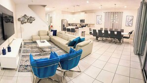 Un salon moderne avec un canapé, des fauteuils bleus, une table basse et un téléviseur.