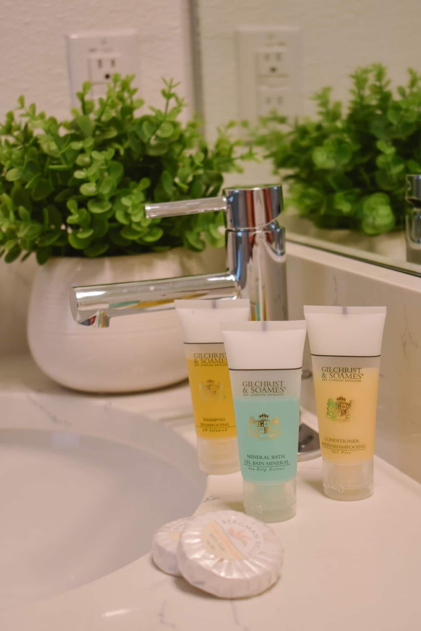 A bathroom with a white sink, a mirror, and three toiletry bottles labeled 'Gilchrist & Soames' on a marble countertop.
