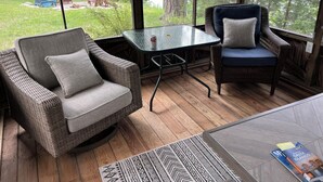A cozy room with wicker furniture, a glass table, and a view of a forested area. - Perfect Cabin on Pokegama Lake (Grand Rapids)