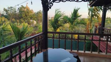A balcony with a glass table, wooden railing, and a view of greenery and a building in the background.