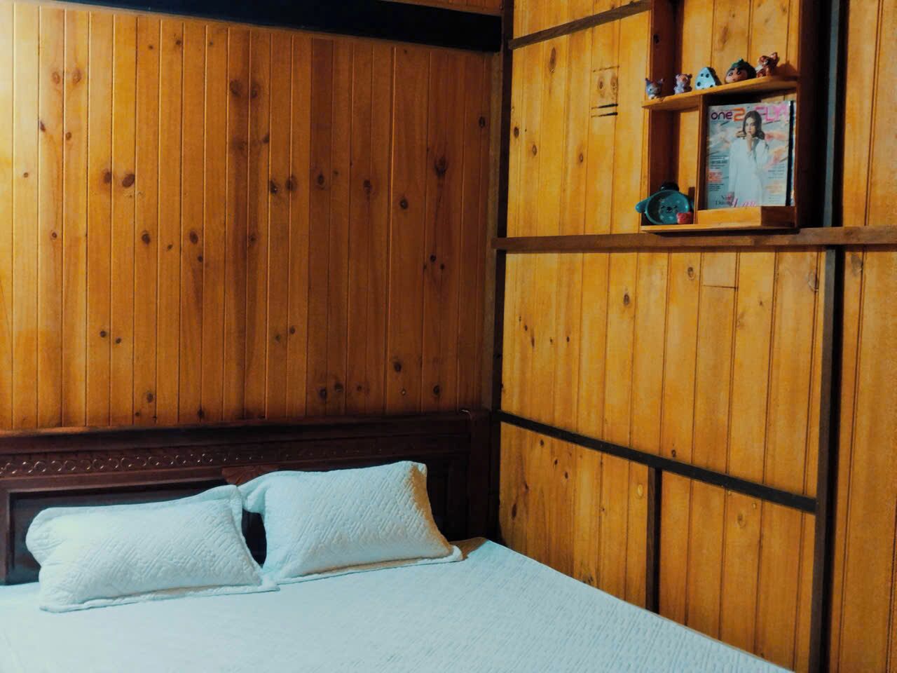 Een kamer met houten lambrisering, een bed, een plank met decoratieve objecten en een lijst met een foto aan de muur.