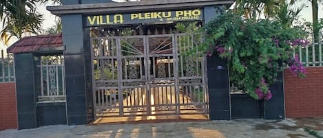 Una entrada con reja a Villa Pleiku Phô, con techo de tejas y un letrero sobre la puerta.