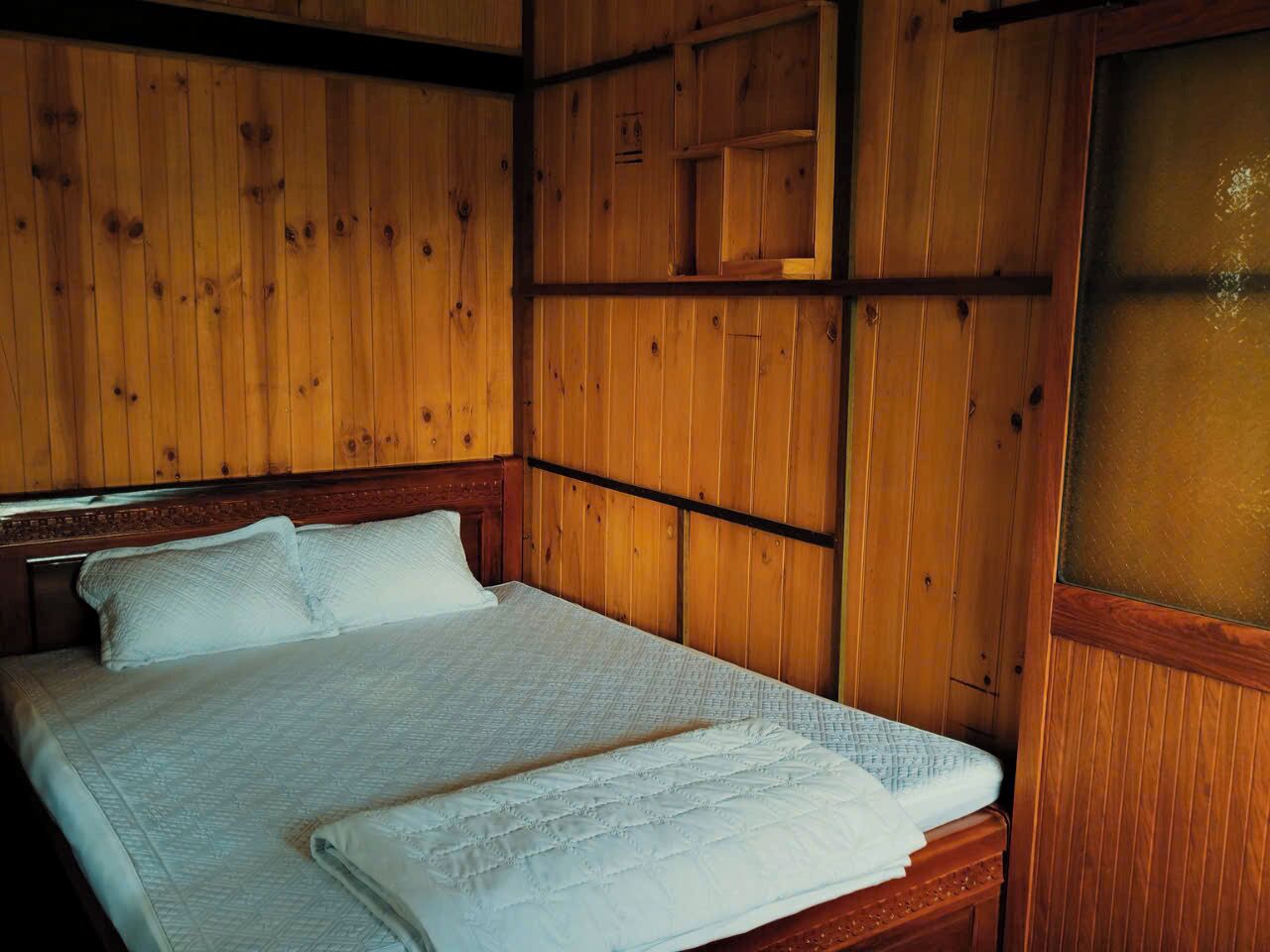 A wooden-paneled room with a bed, a wooden headboard, and a small wooden shelf above the bed.