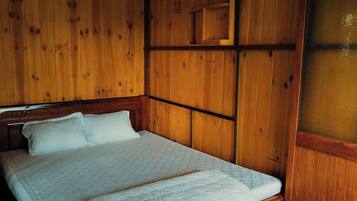 A wooden-paneled room with a bed, a wooden headboard, and a small wooden shelf above the bed.