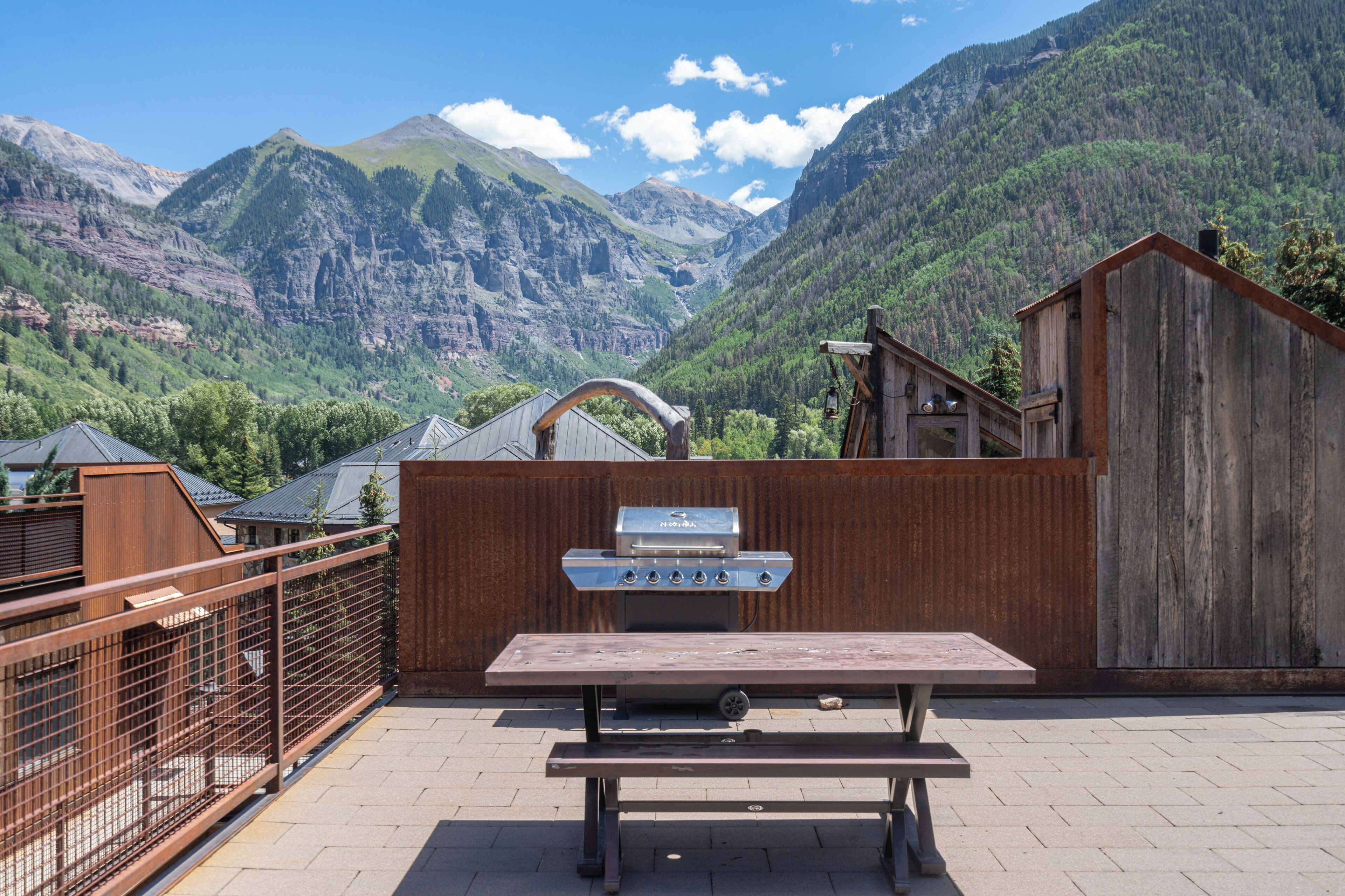 Ein Holz-Essbereich im Freien mit Grill, umgeben von einem Holzzaun und mit Blick auf eine gebirgige Landschaft.