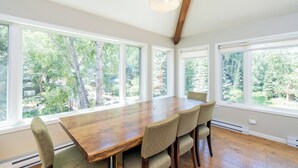 A dining area with a large wooden table, six chairs, and large windows offering a view of trees and a yard. - Amazing Top Floor Ghostrider (Telluride)