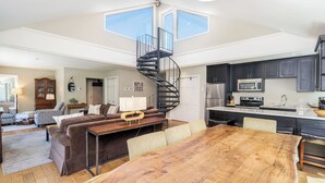 A spacious living area with a wooden dining table, a sofa set, a spiral staircase, and a kitchen with dark cabinets and modern appliances. - Amazing Top Floor Ghostrider (Telluride)