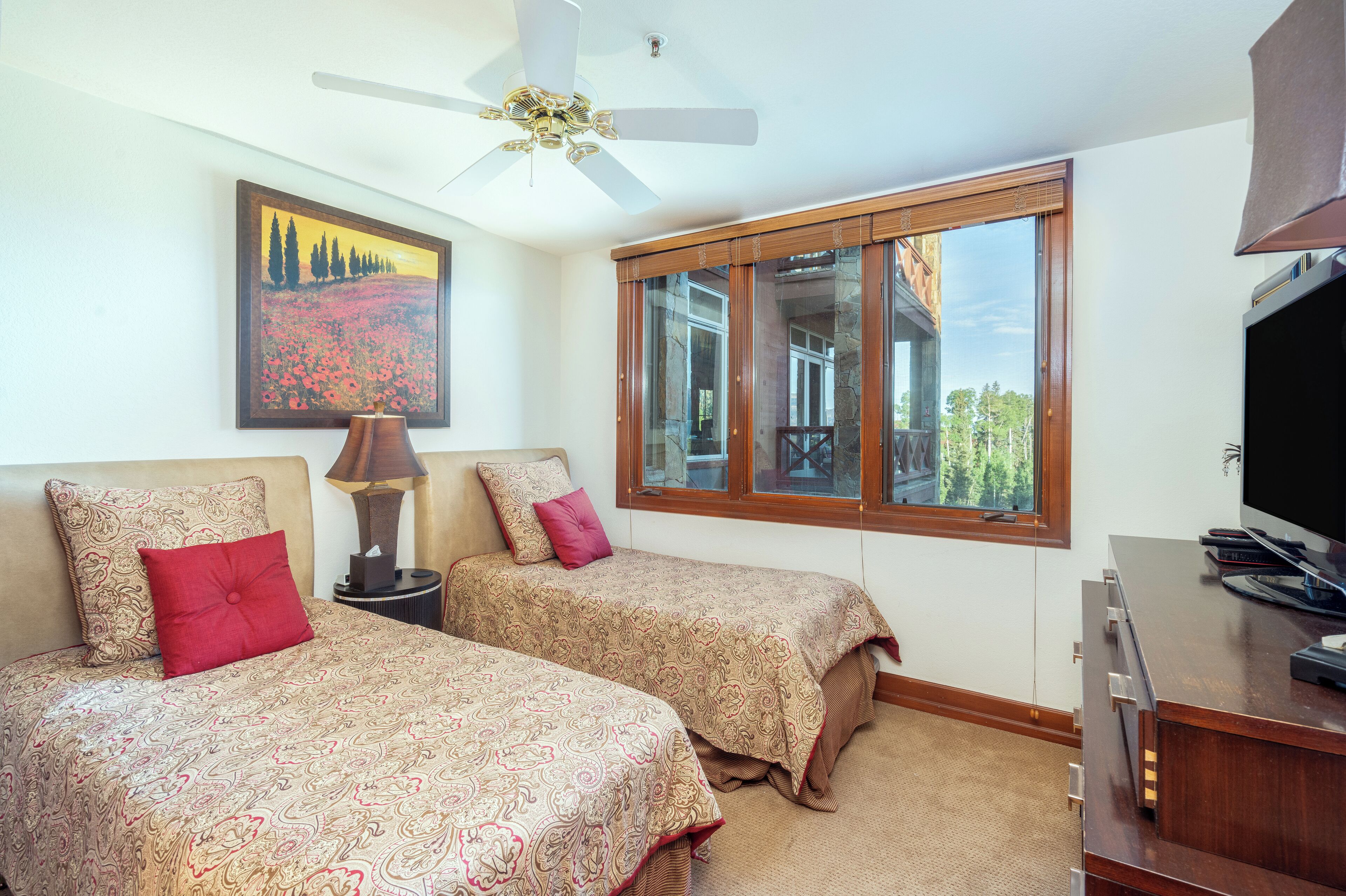 A bedroom with two beds, a ceiling fan, a large window, and a television.