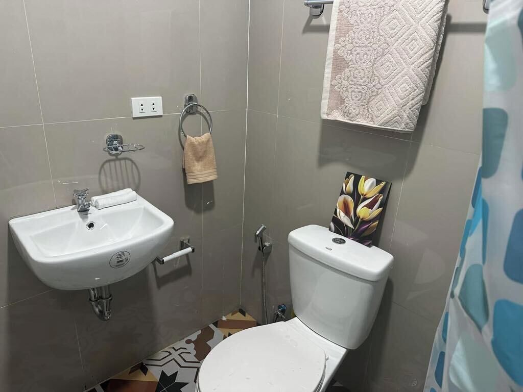 A bathroom with a white sink, toilet, and shower. There is a towel rack with a towel hanging on it. The floor has patterned tiles.