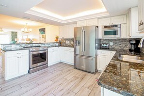 Une cuisine moderne avec des meubles blancs, des appareils en acier inoxydable, un plan de travail en granit et un plancher en bois.
