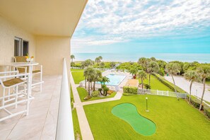 Un balcon avec une chaise et une table blanches, une piscine et une vue sur un terrain de golf.