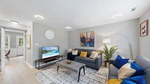 Ett modernt vardagsrum med en grå soffa, ett soffbord och en platt-TV.