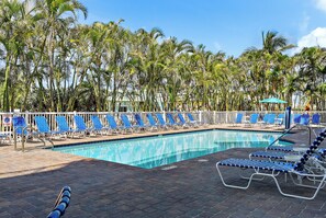 Une piscine avec des chaises longues bleues et des palmiers en arrière-plan.