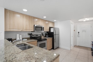 A modern kitchen with granite countertops, stainless steel appliances, wooden cabinets, and a built-in oven. - Peace of Paradise: Pool & Palms View and Beach Access (Treasure Island)
