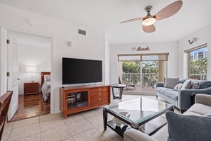 A spacious living room with a flat-screen TV, wooden entertainment unit, and a ceiling fan. - Peace of Paradise: Pool & Palms View and Beach Access (Treasure Island)