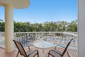 Un balcón con piscina, sillas de descanso y vistas a palmeras y edificios.