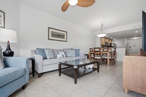 A modern living room with a sofa, coffee table, and dining area. - Peace of Paradise: Pool & Palms View and Beach Access (Treasure Island)