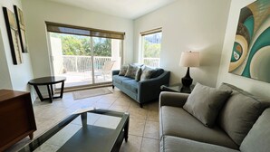 Un salon avec un canapé, une table basse et une lampe. Il y a un balcon avec vue sur la verdure.