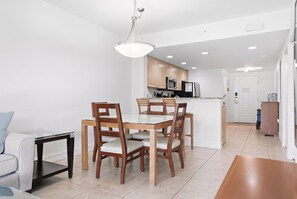 A modern kitchen with wooden cabinets, a central island, and a dining area with a glass table and wooden chairs.