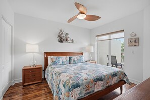 Een slaapkamer met een houten bed, twee nachtkastjes met lampen, een plafondventilator en uitzicht op de omgeving via een schuifdeur.